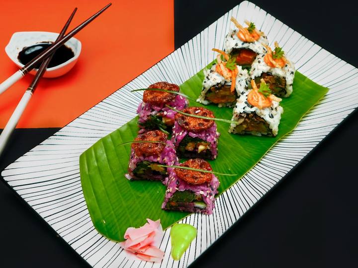 Purple rice sushi rolls with lotus chips and white uramaki on a black-striped plate